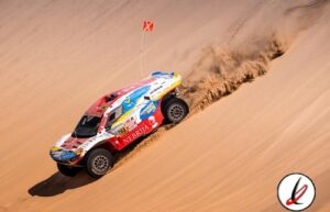Vehículo de rally raid en dunes de arena, en carrera de off-road en Lanzarote, piloto con bandera, tierra y arena en el fondo, movimiento y desafío.