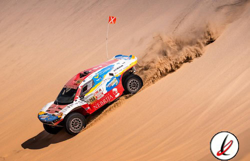 Vehículo de rally raid en dunes de arena, en carrera de off-road en Lanzarote, piloto con bandera, tierra y arena en el fondo, movimiento y desafío.