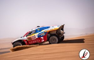 Piloto de rally raid conduciendo un vehículo en el desierto de Lanzarote, con arena y dunas de fondo.