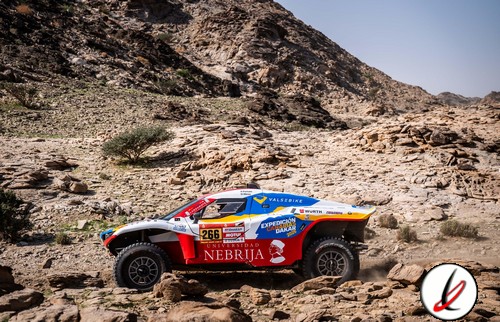 Un vehículo de rally en terreno rocoso en Lanzarote, con colores rojo, azul y blanco, destacando por su diseño aerodinámico y neumáticos adaptados al off-road, en plena competición.