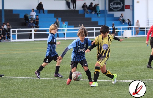 Una jugadora infantil en acción durante un partido de fútbol en un campo de césped artificial. Los niños lucen sus camisetas de diferentes equipos y están luchando por el control del balón.