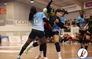 1. Jugadoras de balonmano en acción durante un partido en interiores, con defensas intentando detener el avance del equipo contrario en la pista.