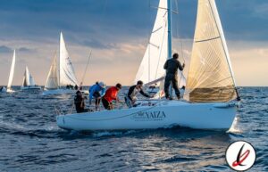 Vela con varias personas en un barco en medio del mar durante una regata al atardecer.
