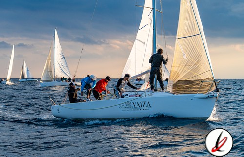 Vela con varias personas en un barco en medio del mar durante una regata al atardecer.