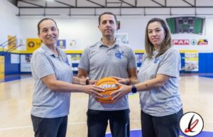 1. Tres personas en una cancha de baloncesto, una mujer y dos hombres, sosteniendo un balón de baloncesto en un entorno de gimnasio cubierto.
