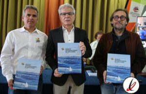 Campeones de la Regata Internacional de San Ginés en Lanzarote con trofeos y certificados, en un evento celebrado en un salón con cortinas verdes y fondo con logos y pantalla digital.