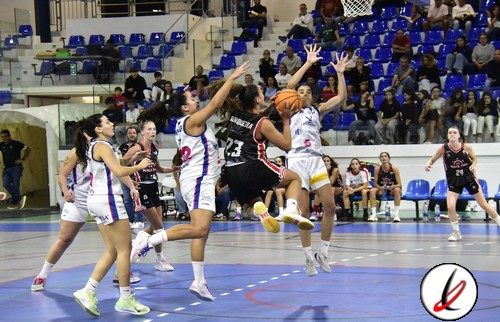 Baloncesto femenino en acción en una cancha cubierta, con jugadoras en movimiento, algunas saltando y esperando el balón, en un partido con espectadores en las gradas del estadio en Lanzarote.