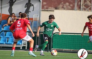 Una jugadora con camiseta verde controlando el balón mientras es presionada por dos jugadores con camiseta roja en un partido de fútbol.