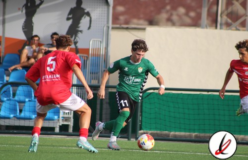 Una jugadora con camiseta verde controlando el balón mientras es presionada por dos jugadores con camiseta roja en un partido de fútbol.