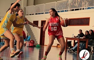 Jugadora de baloncesto con camiseta roja enfrentándose a jugadoras rivales en un partido femenino en una cancha cubierta.