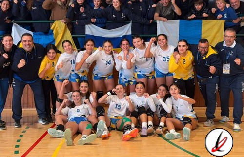Jugadoras de voleibol del equipo femenino posando con celebración en el gimnasio, acompañadas por entrenadores y personal en el fondo.