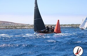 Velero deportivo navegando en el mar con tripulación y boya señalizadora, en Lanzarote.
