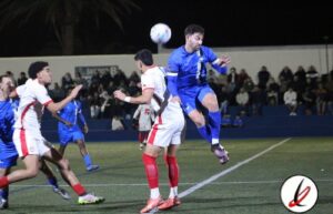 1. Jugadores de fútbol en acción durante un partido nocturno en Lanzarote, con estadio iluminado y espectadores en las gradas.