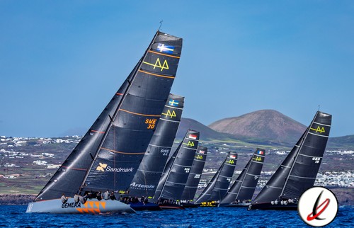 Velero de regata con varias embarcaciones en competición en Lanzarote, fondo de montañas y cielo despejado.