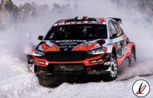 Coche de rally en nieve, con logotipos y colores naranja, negro y blanco, en plena carrera en un entorno helado y con espectadores al fondo.