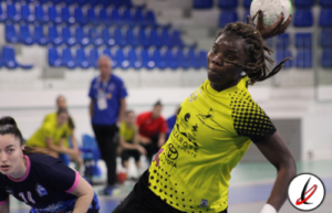 Jugadora de balonmano en acción lanzando el balón en un partido en un pabellón deportivo.