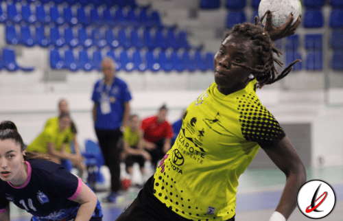 Jugadora de balonmano en acción lanzando el balón en un partido en un pabellón deportivo.