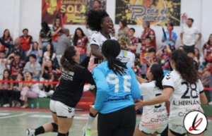 Jugadoras de voleibol celebrando en una cancha cubierta con público en las gradas.