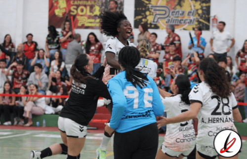 Jugadoras de voleibol celebrando en una cancha cubierta con público en las gradas.