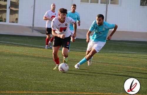 Futbolistas en acción durante un partido en un campo de césped artificial, con jugadores en camiseta blanca y camiseta azul, y un árbitro en el fondo.