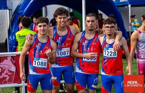 Atletas de atletismo en la línea de salida en Lanzarote, con ropa deportiva roja y azul, sonriendo y posando juntos antes de la carrera en un evento al aire libre.