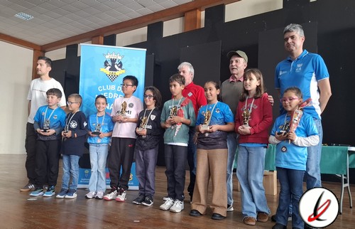 Grupo de niños y adultos en una ceremonia de premiación en un evento deportivo en un salón cubierto.