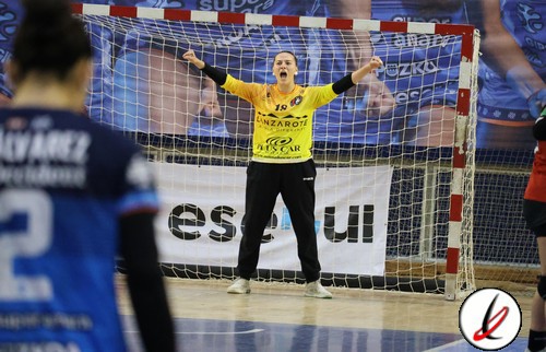 Guardameta en acción durante un partido de balonmano, con los brazos extendidos frente a la portería en un pabellón deportivo.