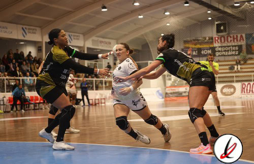 Jugadoras de voleibol en acción en un partido en interiores, con una jugadora en el centro intentando bloquear o recibir el balón mientras las otras dos se preparan para la jugada.