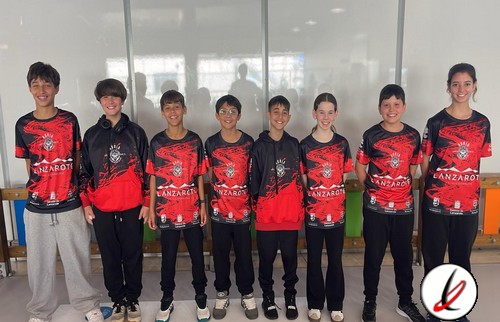 Campeones de un equipo juvenil de baloncesto en una cancha cubierta, con uniformes negros y rojos, sonriendo y posando juntos después de un partido o entrenamiento.