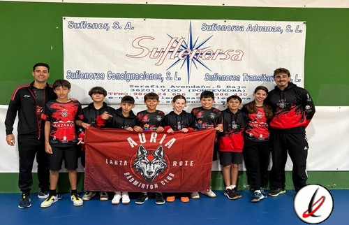 Grupo de jóvenes jugadores de bádminton con sus entrenadores en una pista cubierta, sosteniendo una bandera de su club en Lanzarote.