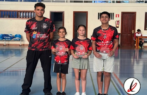 Cuatro jóvenes deportistas con camisetas de bádminton en un gimnasio, sosteniendo raquetas y posando para la foto.