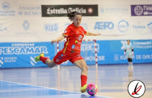 Balón de fútbol sala rosa y morado en un partido de fútbol sala femenino. La jugadora, con uniforme rojo, está en movimiento en la pista, con un fondo de anuncios y un portero en la portería.