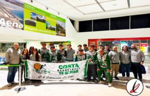 Cesta de baloncesto con jugadores y entrenadores del equipo Costa Basket Teguise en aeropuerto de Lanzarote. Grupo de deportistas con ropa deportiva, algunos con gafas y mascarillas, sosteniendo una p.