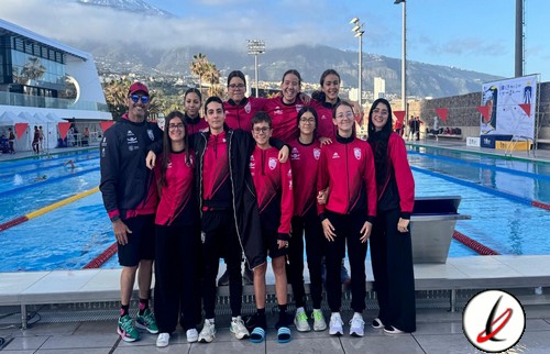 Equipo femenino de natación posando junto a la piscina en un evento deportivo en Lanzarote, con fondo de montañas y cielo despejado.