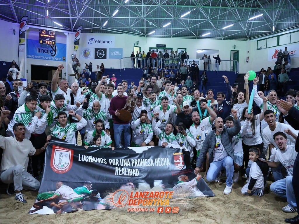Grupo de aficionados y jugadores en un estadio cubierto, celebrando con una pancarta y balón, en un evento deportivo en Lanzarote.