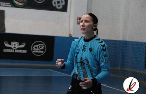 Jugadora de fútbol sala en acción en un partido en interiores, vestida con uniforme azul y número 16, en una cancha cubierta con paredes blancas y anuncios publicitarios.