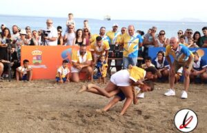 Competidores en una carrera de lucha en la playa con público y jueces observando, en Lanzarote.