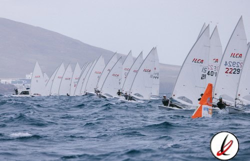 Navegantes en regata de vela en el mar con varias embarcaciones y velas blancas, en un día nublado y con olas moderadas.