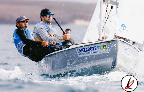 1. Dos regatistas en un velero pequeño navegando a alta velocidad en el mar, con banderas y logos de Lanzarote en la embarcación, bajo un cielo nublado.
