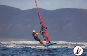 Viento en vela, deportista practicando windsurf en el mar con montañas al fondo.