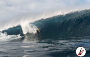 Remolque de surfista en una gran ola en el océano, con cielo nublado de fondo.