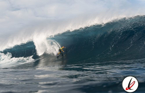 Remolque de surfista en una gran ola en el océano, con cielo nublado de fondo.
