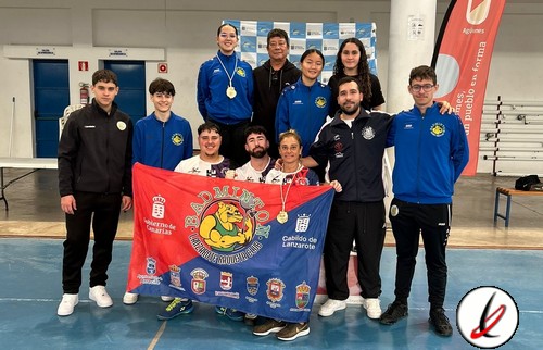Grupo de deportistas con medallas y bandera en un gimnasio cubierto, celebrando un logro deportivo en Lanzarote.