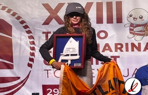 Mujer con gafas y gorra sosteniendo un trofeo en un evento deportivo, con fondo de cartel y personajes de dibujos animados.