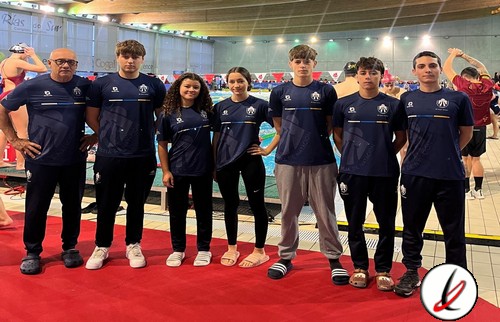 Grupo de siete jóvenes deportistas con entrenador en un entorno deportivo cubierto, vistiendo camisetas de equipo azul oscuro con detalles blancos.