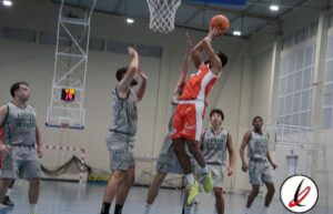 Jugador de baloncesto en acción, saltando para encestar en una cancha cubierta con otros jugadores en defensa.