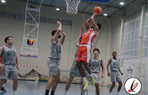 Jugador de baloncesto en acción, saltando para encestar en una cancha cubierta con otros jugadores en defensa.