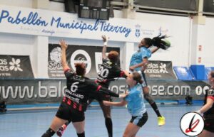 Jugadoras de balonmano en acción durante un partido en el Pabellón Municipal Titerroy, con una jugadora en azul saltando para lanzar mientras las oponentes intentan bloquear.