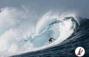 Remojón de surfista en una ola gigante en el océano, con cielo nublado de fondo.