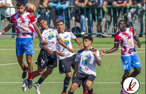 Jugadores de fútbol en acción durante un partido en un campo de césped, con público en las gradas al fondo.